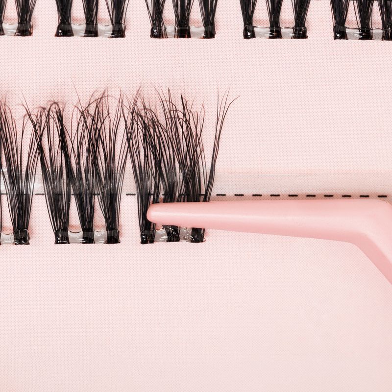 False eyelashes on a pink background with a hand holding one lash.