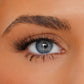 Close-up of a blue-gray eye with long black eyelashes, a filled eyebrow, and light makeup on smooth skin.