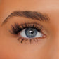 Close-up of a person's eye with long, dark, curled eyelashes and a neatly shaped eyebrow on warm-toned skin.