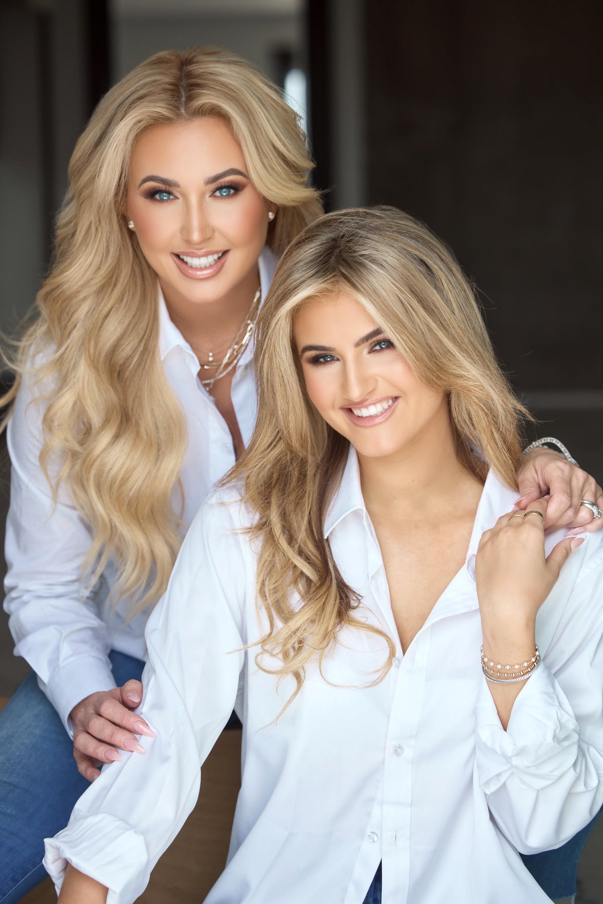 Two women wearing white shirts posing together indoors.