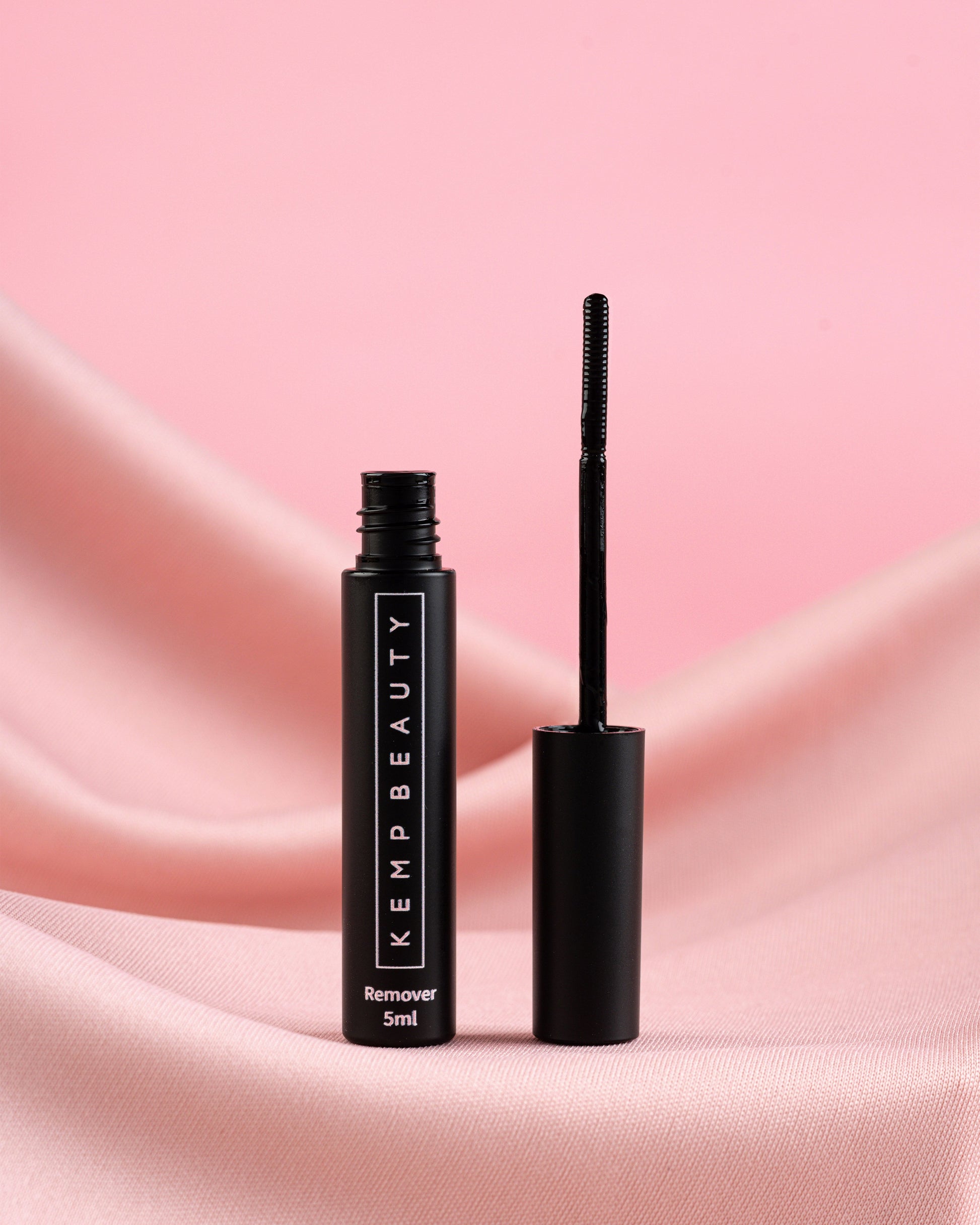Black mascara tube with brush on a pink fabric background, featuring Kemp Beauty branding.