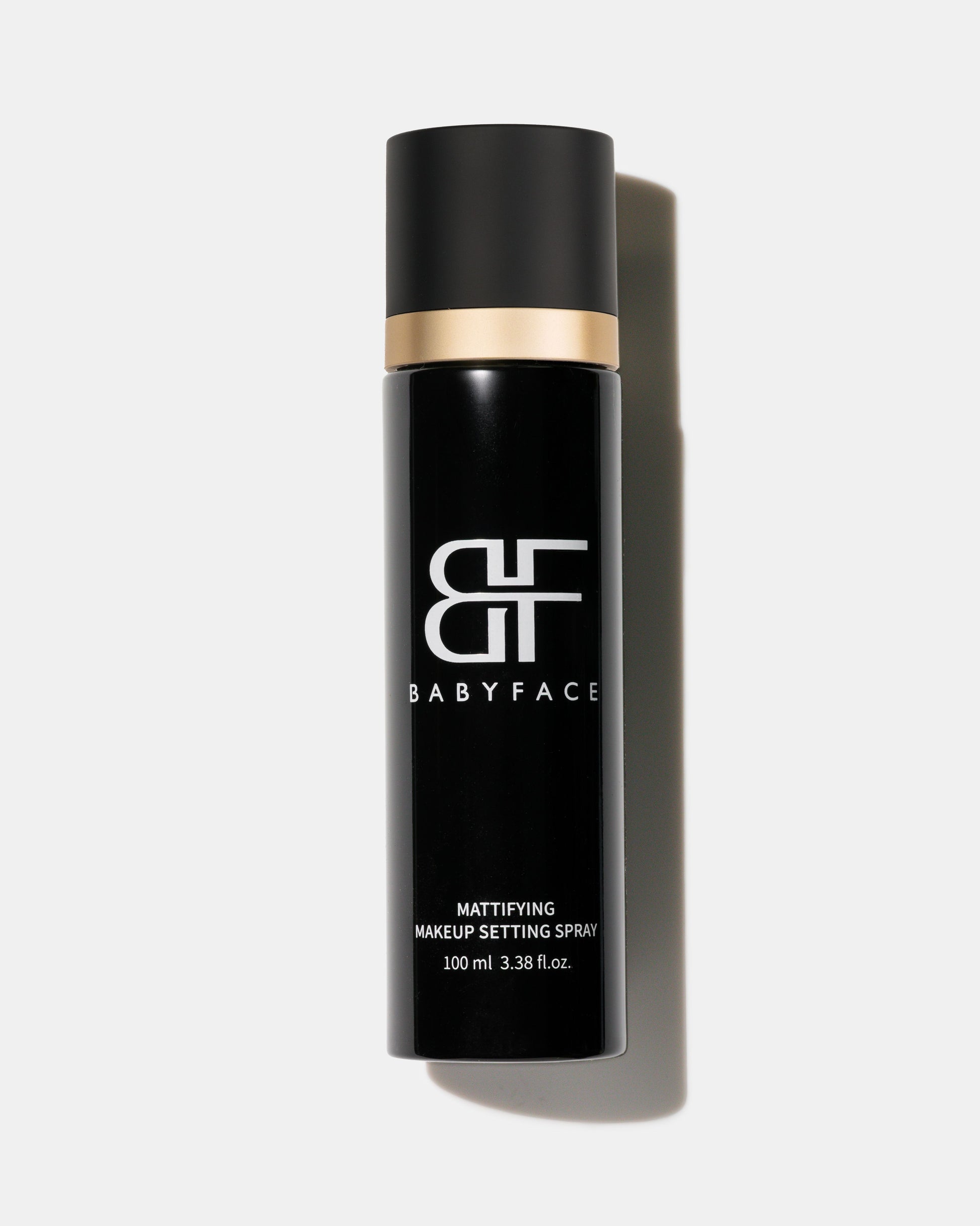 Black makeup setting spray bottle with gold cap on a white background